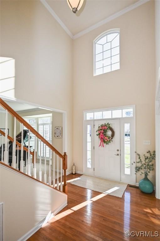 foyer with hardwood / wood-style flooring, crown molding, and a towering ceiling