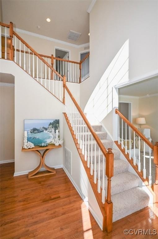 staircase featuring a high ceiling, ornamental molding, and hardwood / wood-style floors