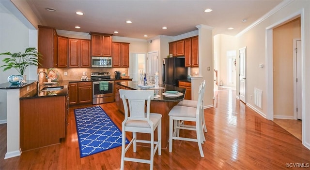 kitchen with a kitchen bar, appliances with stainless steel finishes, decorative backsplash, a kitchen island, and sink