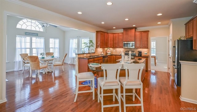 kitchen featuring appliances with stainless steel finishes, a kitchen bar, tasteful backsplash, kitchen peninsula, and light wood-type flooring