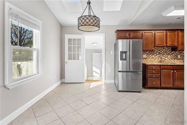 kitchen featuring sink, hanging light fixtures, light tile patterned floors, light stone counters, and stainless steel fridge with ice dispenser