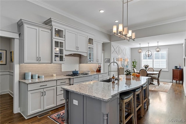 kitchen featuring stainless steel gas cooktop, sink, decorative light fixtures, a center island with sink, and light stone countertops