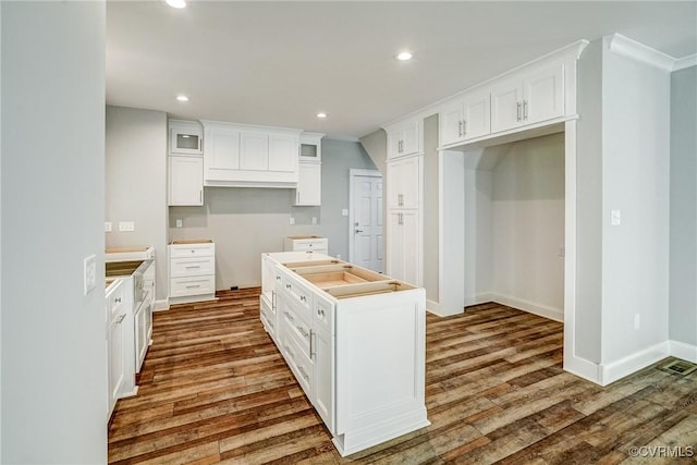 kitchen with white cabinets, a center island, ornamental molding, and hardwood / wood-style flooring