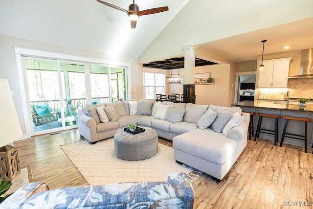 living room featuring light wood-type flooring, ceiling fan, high vaulted ceiling, and decorative columns