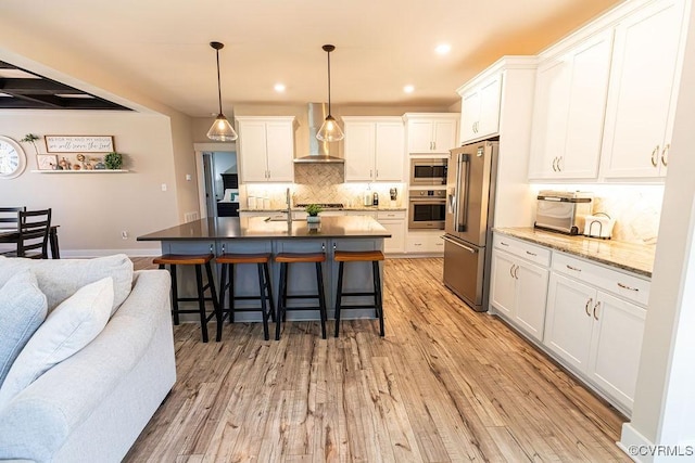 kitchen with wall chimney range hood, stainless steel appliances, white cabinets, and pendant lighting