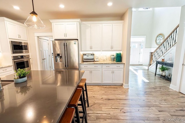 kitchen with white cabinets, light hardwood / wood-style floors, hanging light fixtures, and appliances with stainless steel finishes