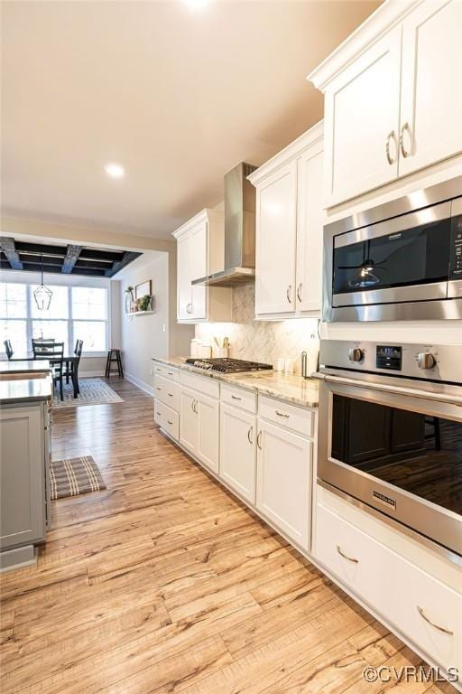 kitchen featuring wall chimney range hood, light wood-type flooring, white cabinets, and tasteful backsplash