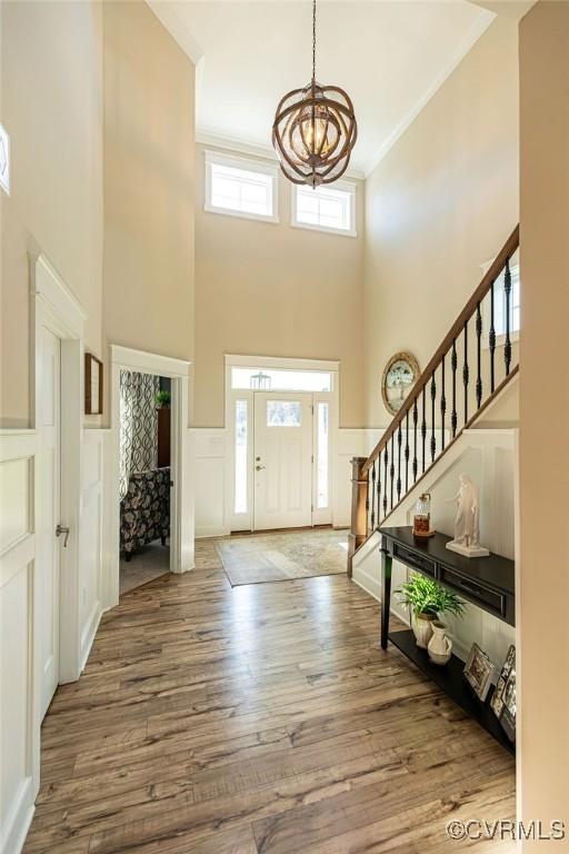 foyer entrance with hardwood / wood-style flooring, a towering ceiling, a notable chandelier, and ornamental molding