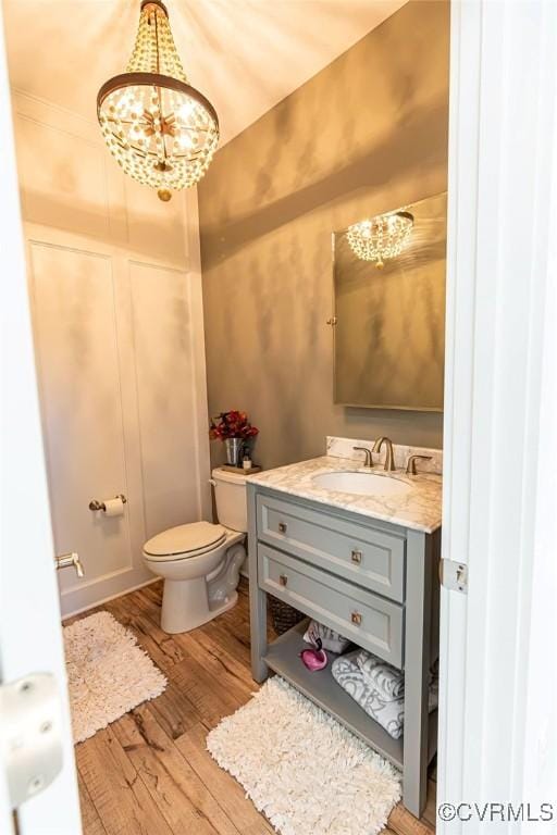 bathroom with hardwood / wood-style floors, toilet, a notable chandelier, and vanity