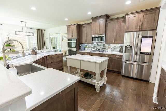 kitchen with hanging light fixtures, sink, a kitchen island, dark wood-type flooring, and stainless steel appliances