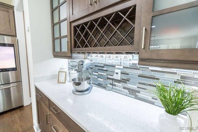 kitchen with dark wood-type flooring, decorative backsplash, stainless steel refrigerator, and light stone counters