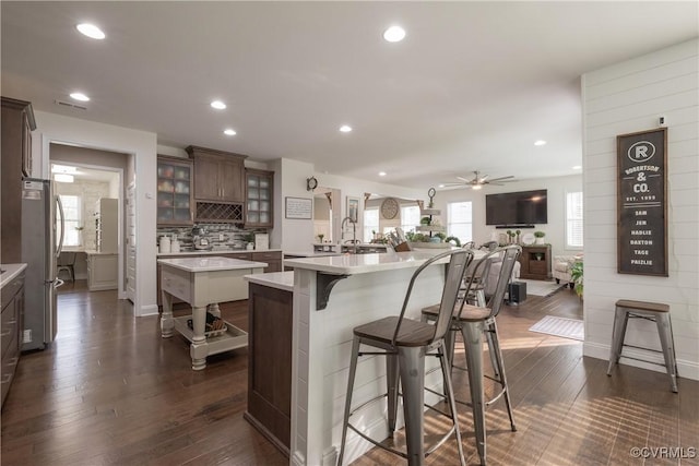 kitchen with a kitchen island, a breakfast bar area, stainless steel fridge, decorative backsplash, and dark wood-type flooring