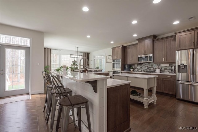 kitchen with stainless steel appliances, hanging light fixtures, a center island with sink, and backsplash