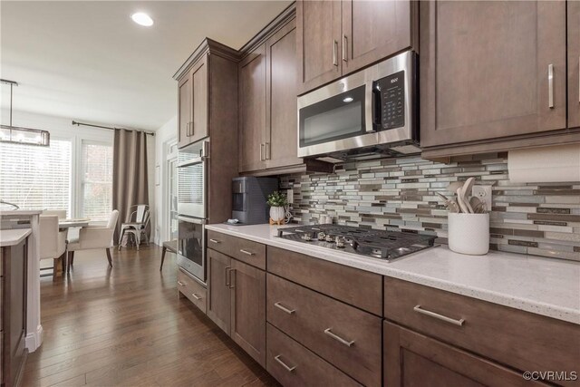 kitchen with tasteful backsplash, stainless steel appliances, decorative light fixtures, and dark wood-type flooring