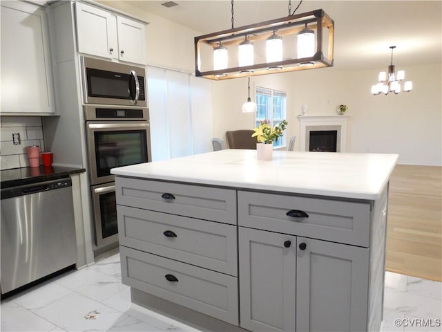 kitchen featuring appliances with stainless steel finishes, hanging light fixtures, backsplash, and gray cabinets