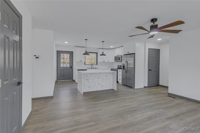 kitchen featuring stainless steel appliances, ceiling fan, pendant lighting, a kitchen island, and white cabinetry