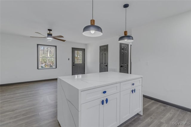 kitchen featuring a center island, ceiling fan, light stone counters, white cabinets, and decorative light fixtures