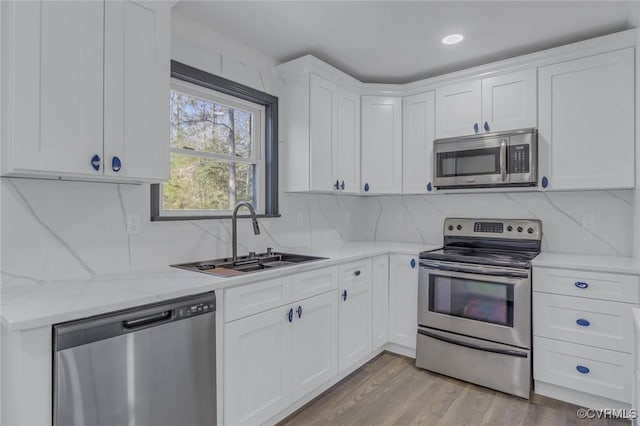 kitchen with appliances with stainless steel finishes, light wood-type flooring, light stone counters, white cabinets, and sink