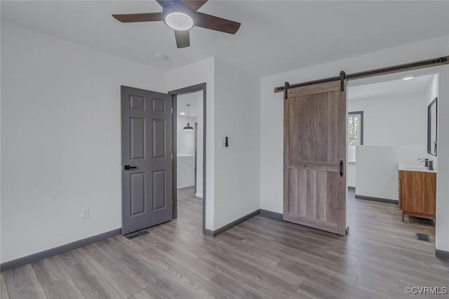 unfurnished bedroom with sink, ceiling fan, a barn door, and light hardwood / wood-style flooring