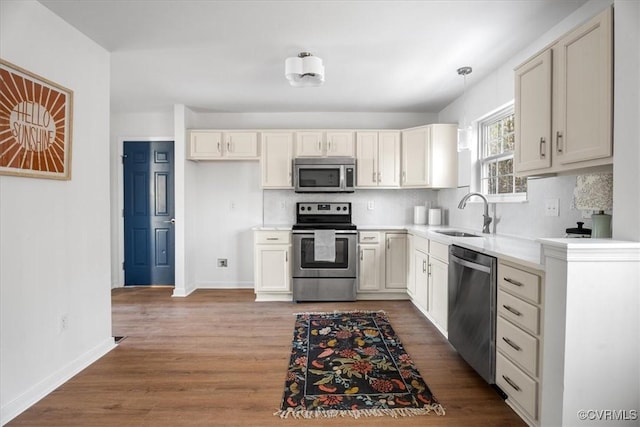 kitchen with sink, stainless steel appliances, decorative light fixtures, and hardwood / wood-style flooring