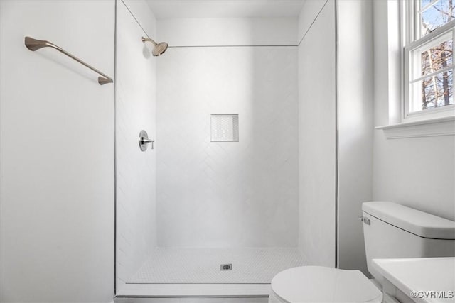 bathroom with toilet, tiled shower, and a wealth of natural light