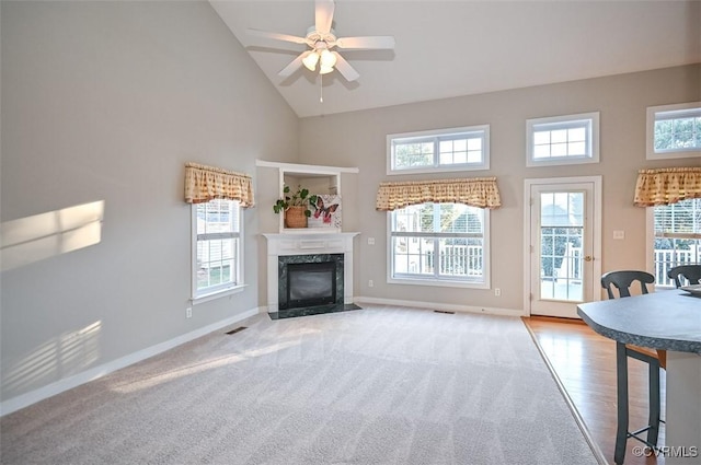 unfurnished living room featuring a high end fireplace, high vaulted ceiling, light colored carpet, and ceiling fan