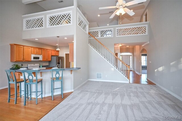 kitchen with white appliances, a kitchen breakfast bar, a towering ceiling, kitchen peninsula, and decorative light fixtures