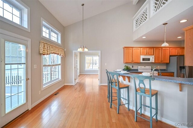 kitchen with white appliances, high vaulted ceiling, hanging light fixtures, and a kitchen bar