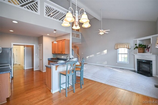 kitchen with a kitchen breakfast bar, light hardwood / wood-style floors, high vaulted ceiling, a fireplace, and ceiling fan with notable chandelier