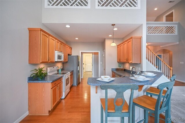 kitchen with stainless steel appliances, a towering ceiling, light wood-type flooring, a breakfast bar area, and pendant lighting