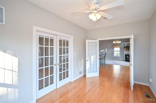 spare room with ceiling fan with notable chandelier, french doors, and light hardwood / wood-style flooring