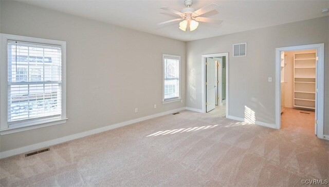 unfurnished bedroom featuring multiple windows, light carpet, ceiling fan, and a spacious closet