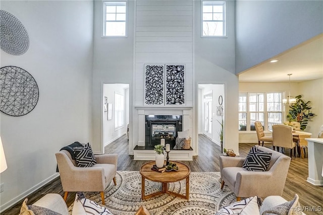 living room with an inviting chandelier, a towering ceiling, hardwood / wood-style flooring, and a high end fireplace