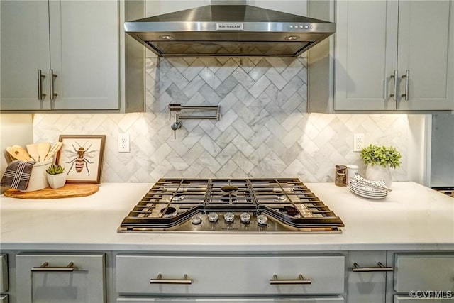 kitchen featuring wall chimney range hood, stainless steel gas stovetop, tasteful backsplash, and gray cabinetry