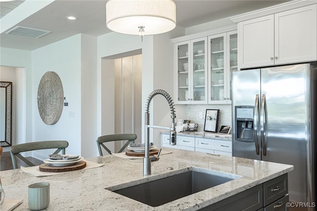 kitchen featuring white cabinets, stainless steel fridge, light stone counters, sink, and tasteful backsplash