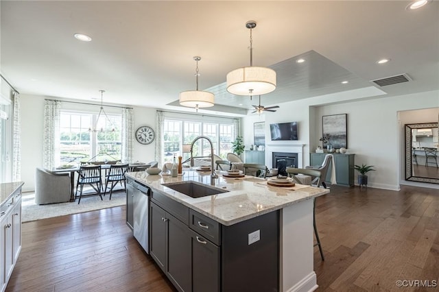 kitchen with dishwasher, dark hardwood / wood-style floors, decorative light fixtures, an island with sink, and sink