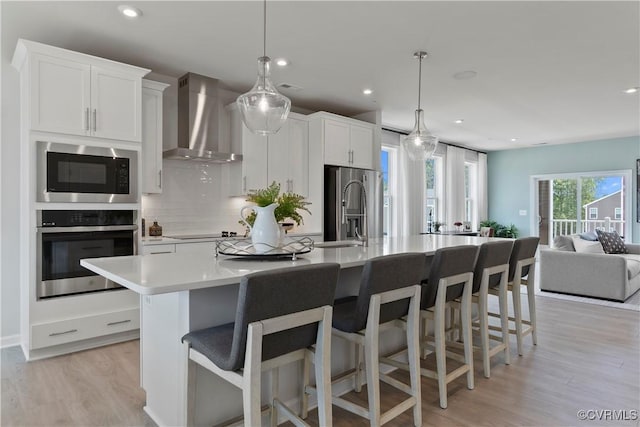 kitchen featuring decorative light fixtures, stainless steel appliances, a spacious island, and wall chimney exhaust hood