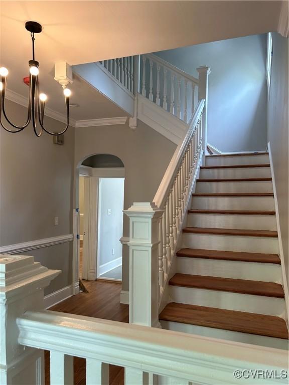 stairs featuring a notable chandelier, ornamental molding, and hardwood / wood-style floors