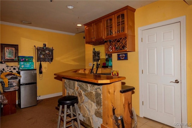 bar with light tile patterned floors, crown molding, and stainless steel fridge