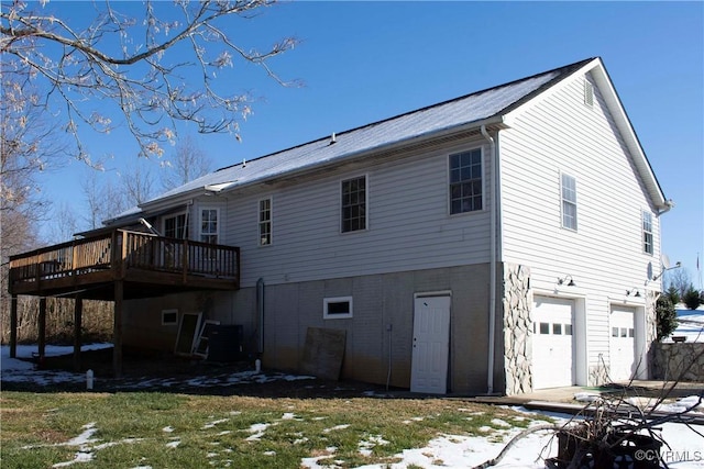 snow covered rear of property featuring cooling unit, a garage, and a wooden deck