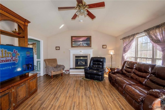 living room featuring vaulted ceiling, a fireplace, light wood-type flooring, and ceiling fan