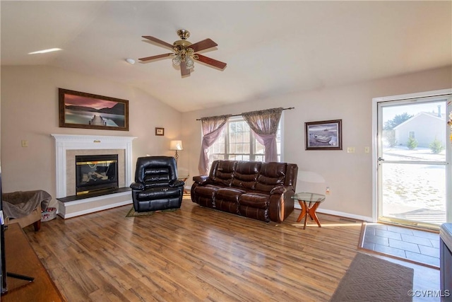 living room featuring vaulted ceiling, hardwood / wood-style flooring, ceiling fan, and a tile fireplace