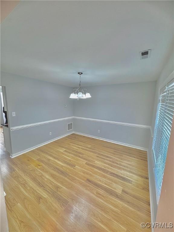 spare room with light hardwood / wood-style floors and a chandelier