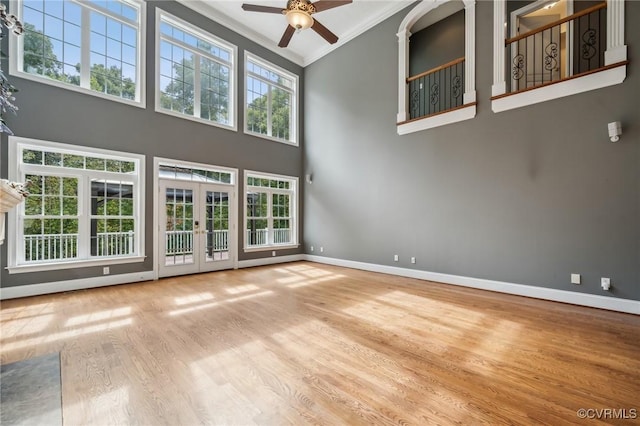 unfurnished living room featuring ceiling fan, crown molding, plenty of natural light, and a high ceiling