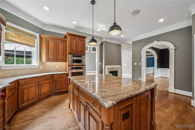 kitchen featuring a center island, wood-type flooring, stainless steel double oven, hanging light fixtures, and light stone countertops