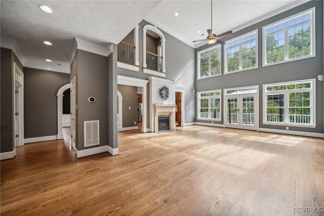 unfurnished living room with a towering ceiling, ceiling fan, crown molding, and wood-type flooring