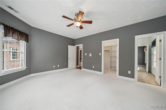 unfurnished bedroom featuring a closet, a walk in closet, ceiling fan, and light carpet