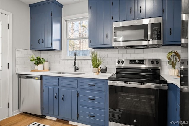 kitchen featuring appliances with stainless steel finishes, blue cabinetry, light wood-type flooring, decorative backsplash, and sink