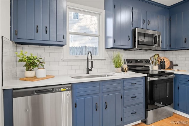 kitchen with stainless steel appliances, light hardwood / wood-style floors, tasteful backsplash, blue cabinetry, and sink