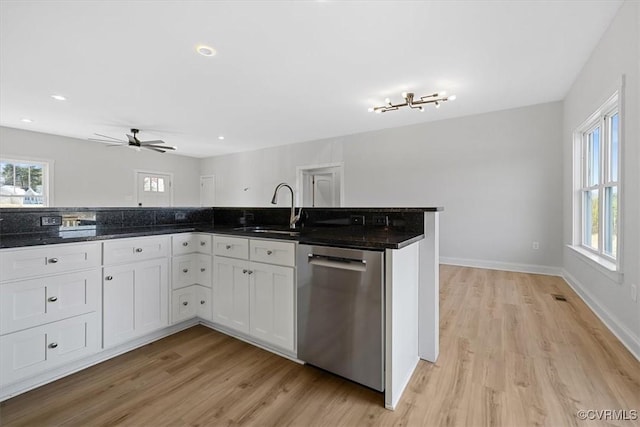 kitchen featuring stainless steel dishwasher, light wood-type flooring, white cabinets, dark stone countertops, and sink